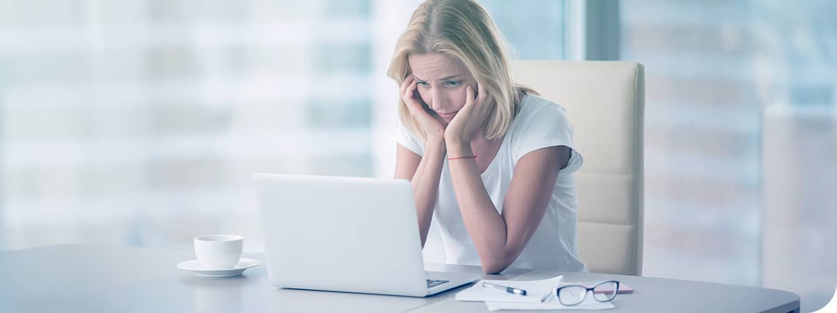 jeune femme blonde l'air découragée assise devant un ordinateur portable